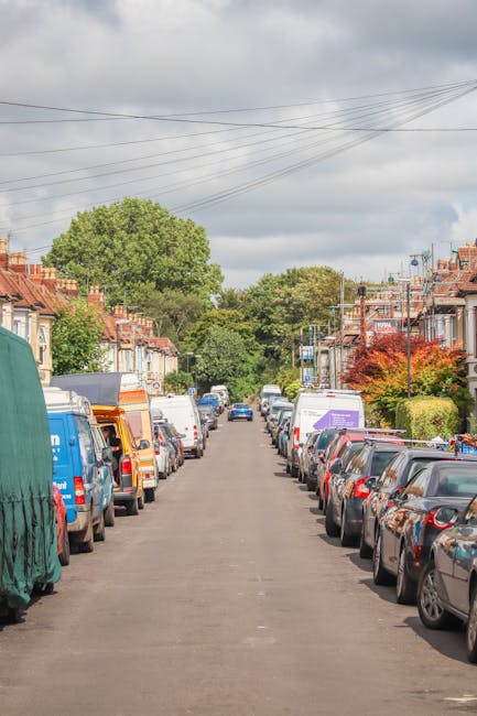 A wide street scene in West Hampstead showing a gentle curve with parked cars lining both sides of the road. Several vehicles are visible, including a silver Audi in the foreground on the right, and a